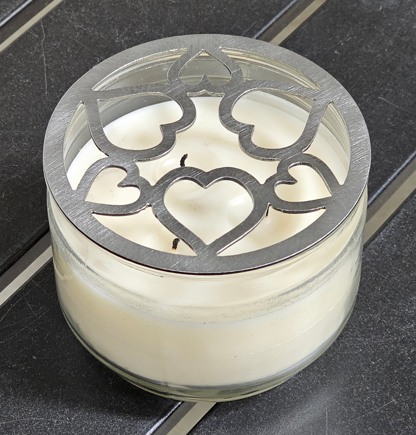 Tangled Hearts metal candle topper featuring intertwined heart design on a lit jar candle