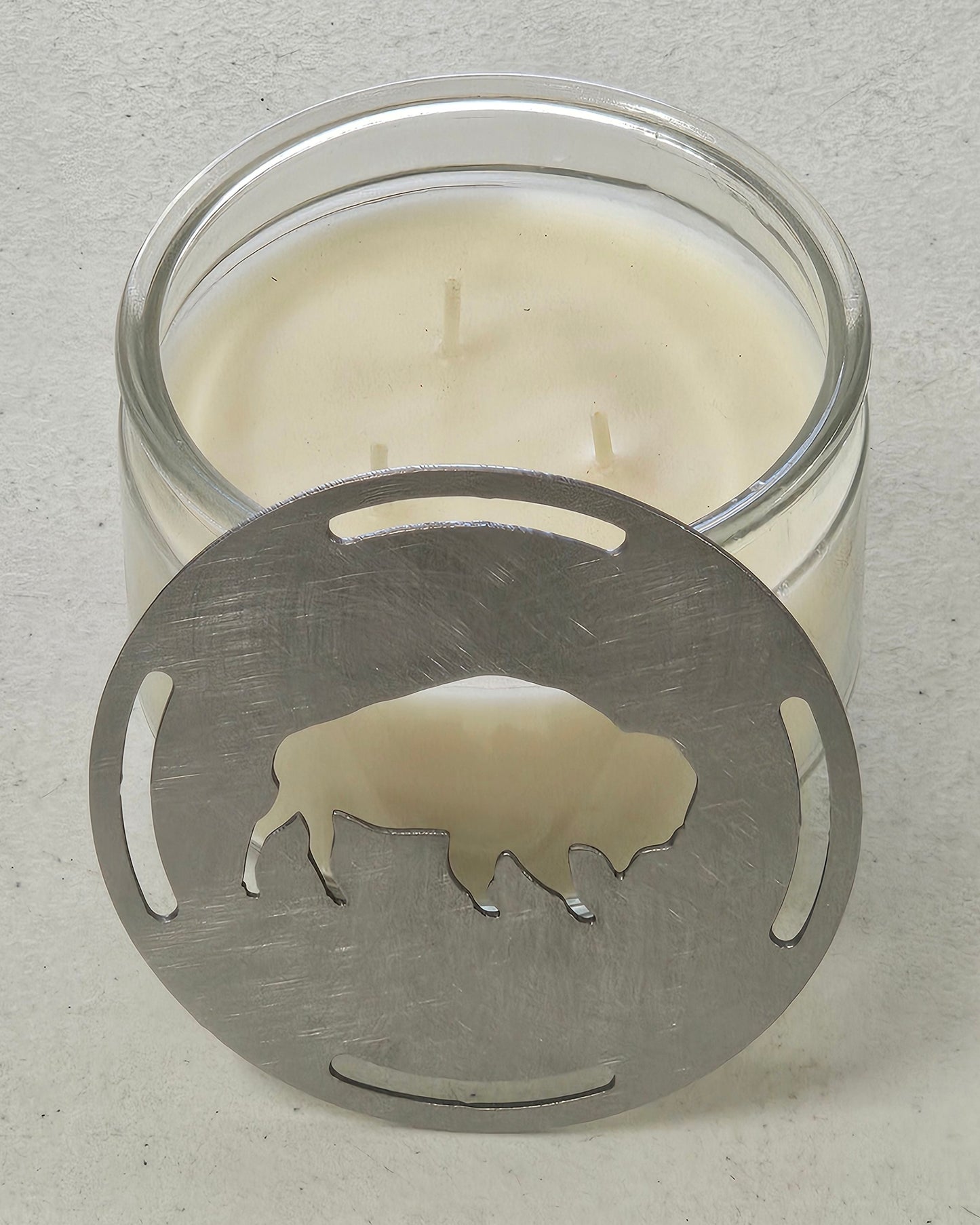 Buffalo candle topper steel lid sitting against a glass jar candle