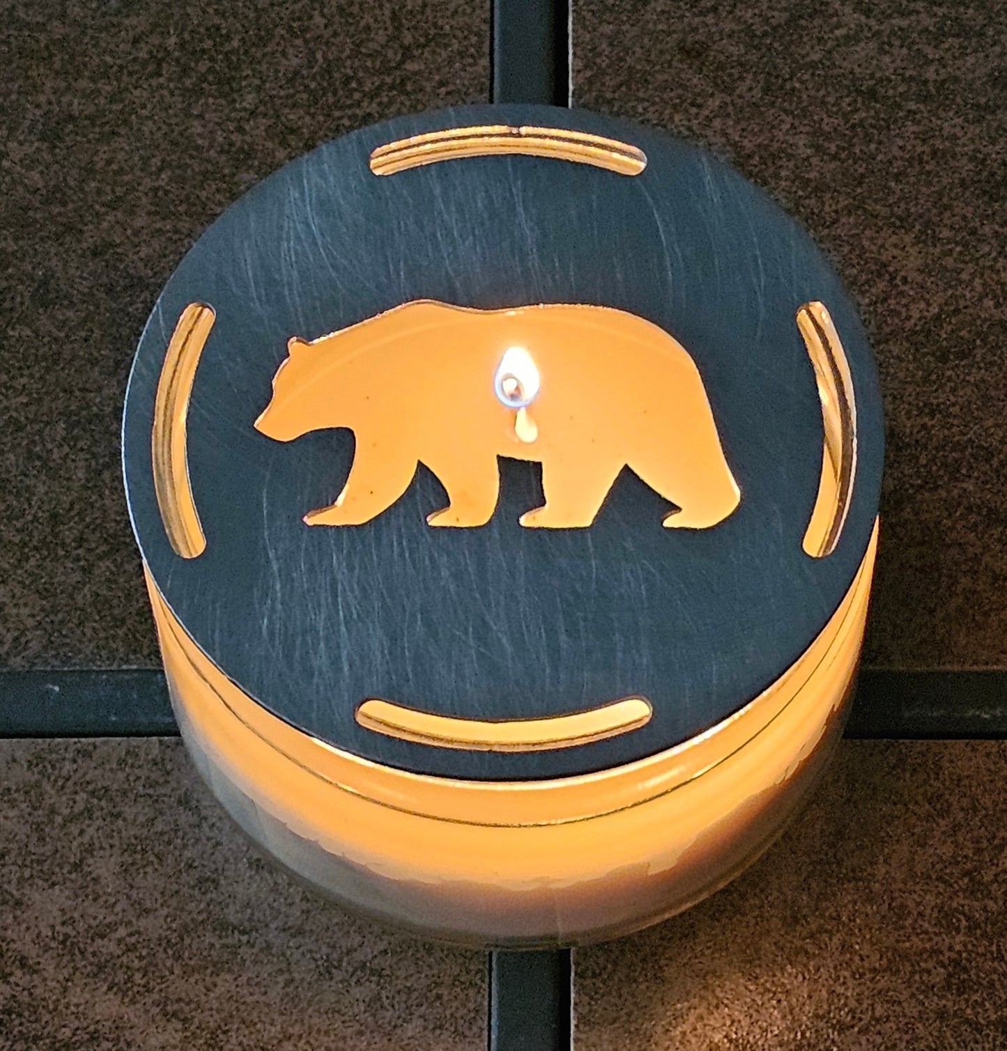 Black flat metal bear candle topper glowing on lit jar candle in rustic cabin decor setting