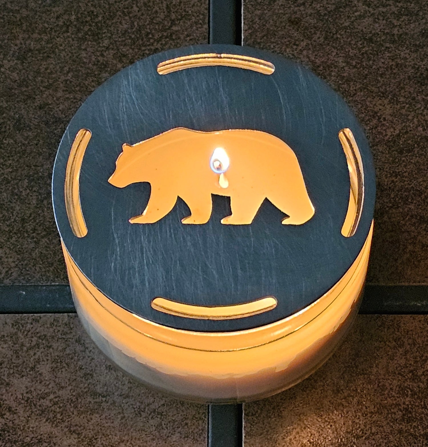 Black flat metal bear candle topper glowing on lit jar candle in rustic cabin decor setting