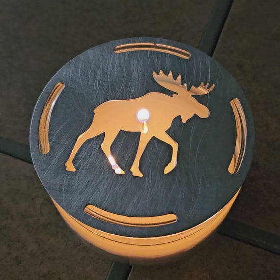Moose candle topper on a lit jar candle creating a warm glowing silhouette, rustic cabin decor